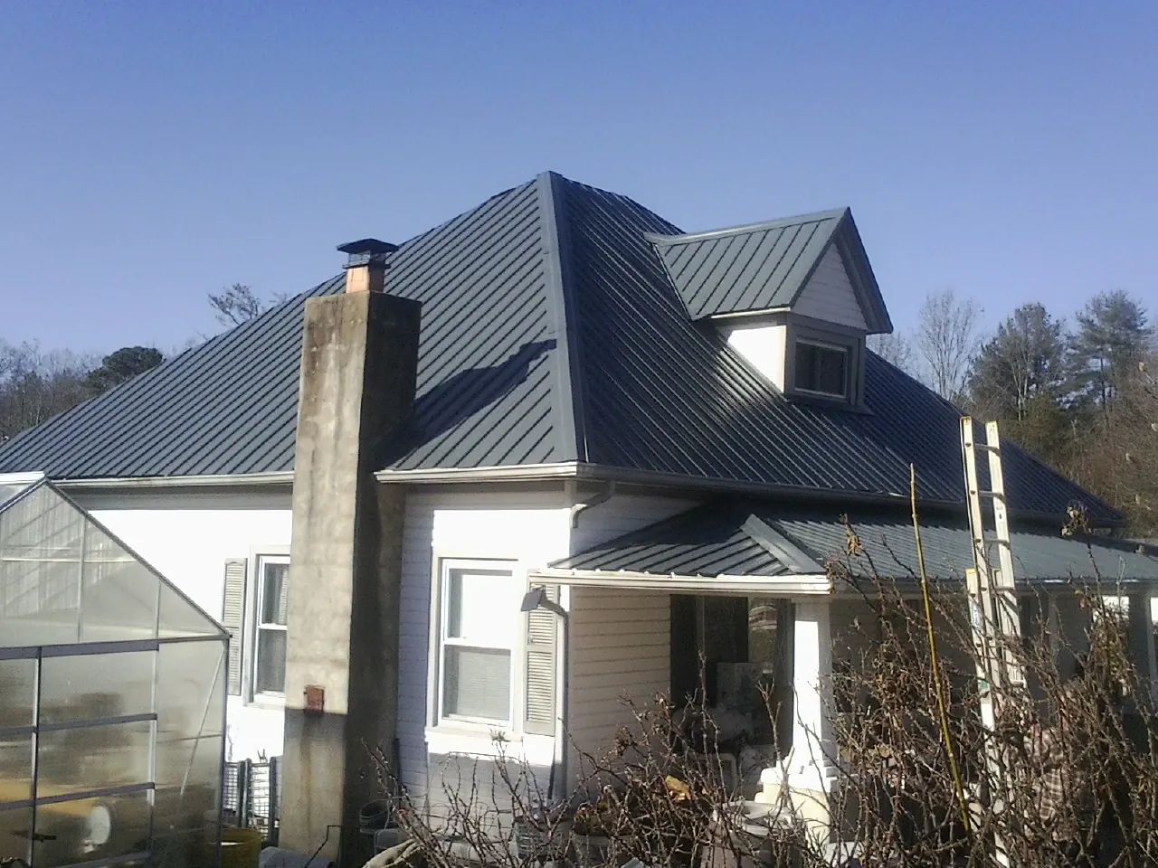 Dark blue standing seam metal roof on a white farmhouse with dormer in Guatay
