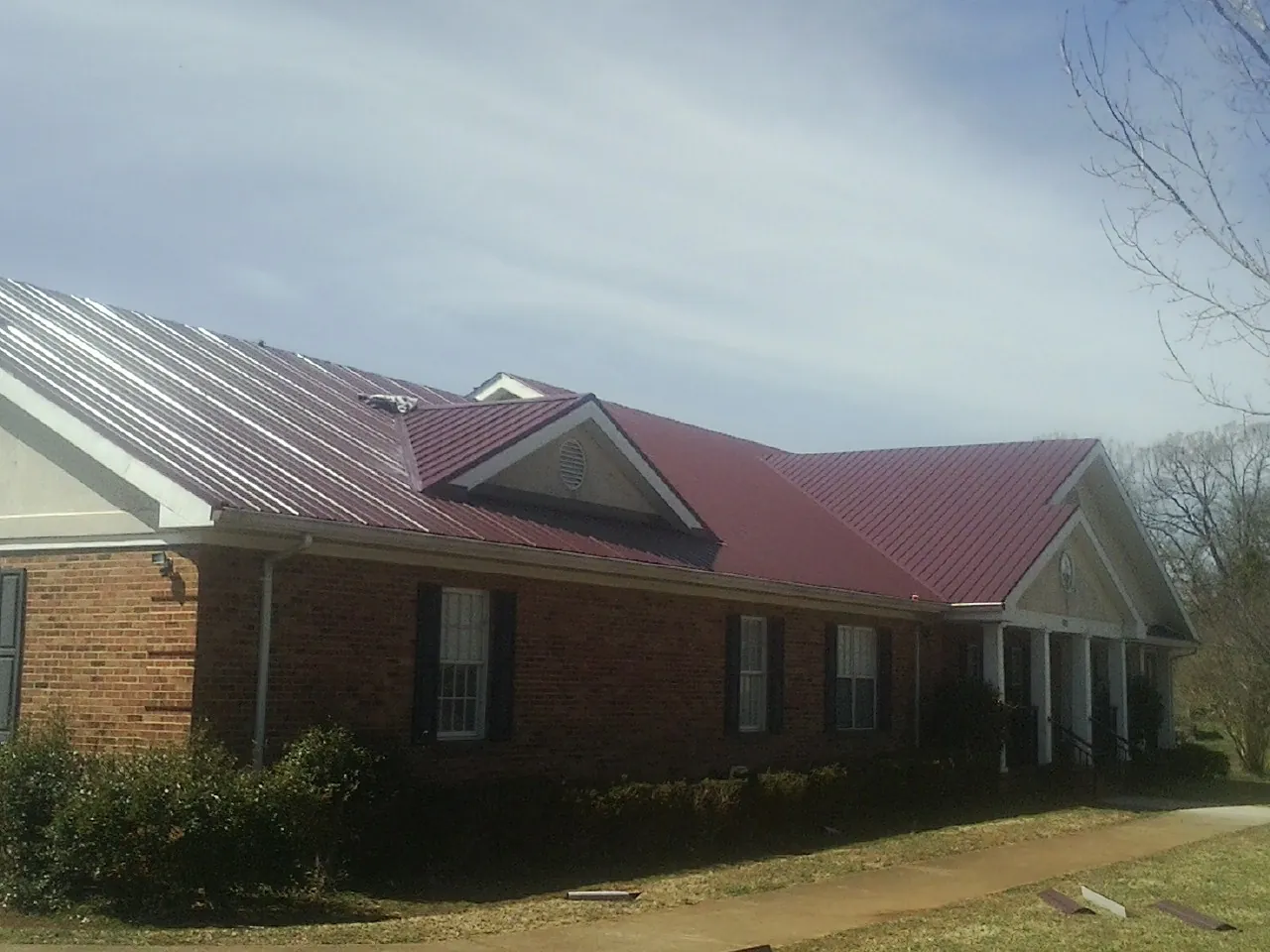 Red metal roof with gabled entries on a long brick building, from a Hail Damage Roof Repair job in Guatay